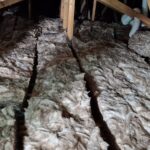 Attic insulated with thick layers of fiberglass batt insulation between wooden beams.