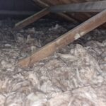 Interior of an attic filled with fluffy insulation material, with wooden beams and partial framing visible.